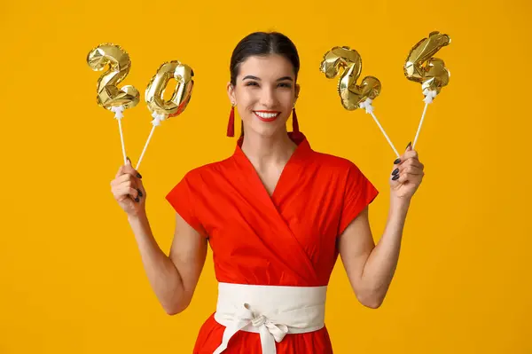Beautiful young happy woman with figure 2024 made of balloons on yellow background. Chinese New Year celebration