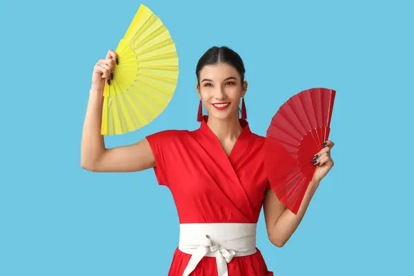 Beautiful young happy woman with fans on blue background. Chinese New Year celebration