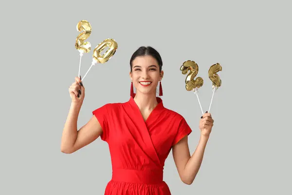 Beautiful young happy woman with figure 2024 made of balloons on grey background. Chinese New Year celebration