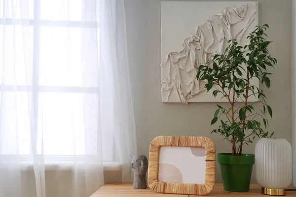 Green plant with frame, lamp and decor on table in room