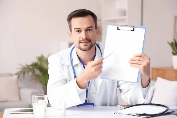 Handsome doctor with clipboard video chatting at home office