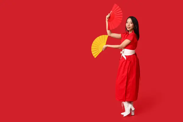 Beautiful young happy Asian woman with fans on red background. Chinese New Year celebration