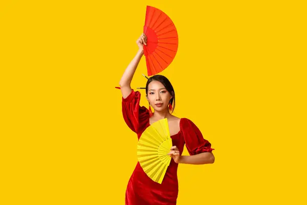 Beautiful young Asian woman with fans on yellow background. Chinese New Year celebration