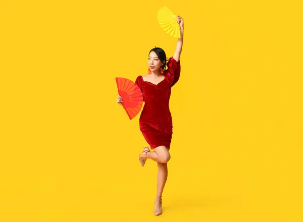 Beautiful young happy Asian woman with fans on yellow background. Chinese New Year celebration