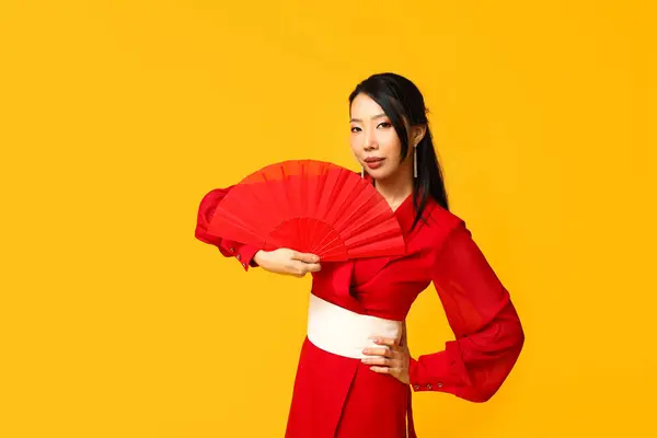 Beautiful young Asian woman with fan on yellow background. Chinese New Year celebration