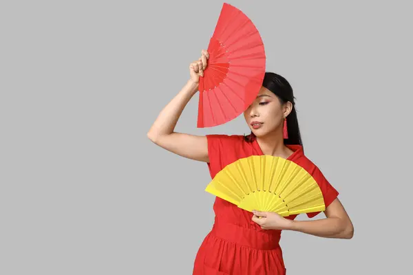 Beautiful young Asian woman with fans on grey background. Chinese New Year celebration