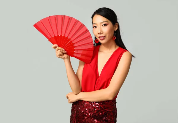 Beautiful young happy Asian woman with fan on grey background. Chinese New Year celebration