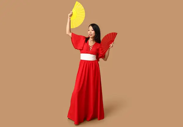 Beautiful young happy Asian woman with fans on brown background. Chinese New Year celebration