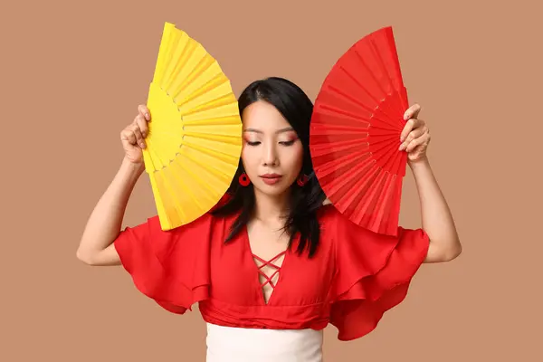 Beautiful young Asian woman with fans on brown background. Chinese New Year celebration