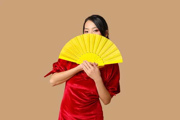 Beautiful young Asian woman with fan on brown background. Chinese New Year celebration