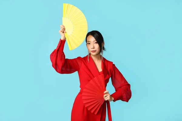 Beautiful young Asian woman with fans on blue background. Chinese New Year celebration