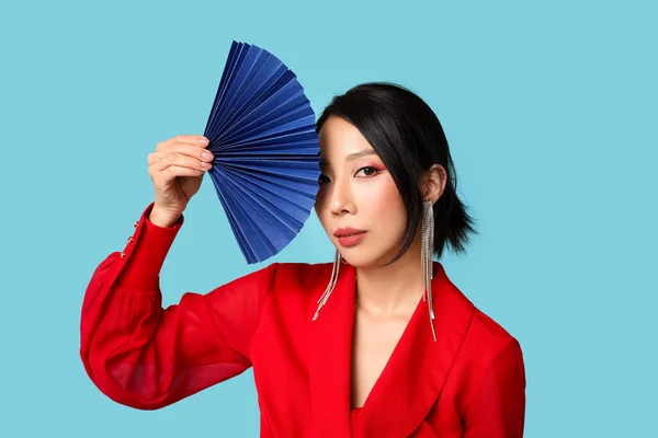 Beautiful young Asian woman with fan on blue background. Chinese New Year celebration