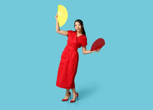 Beautiful young happy Asian woman with fans on blue background. Chinese New Year celebration