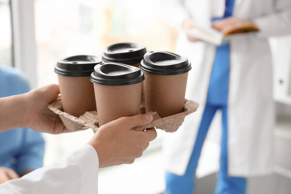 Young doctor with cups of coffee in clinic, closeup