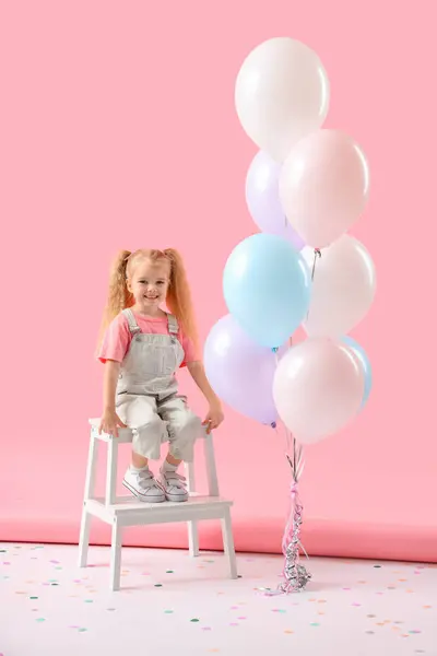 Cute little girl with beautiful balloons sitting on step stool against pink background