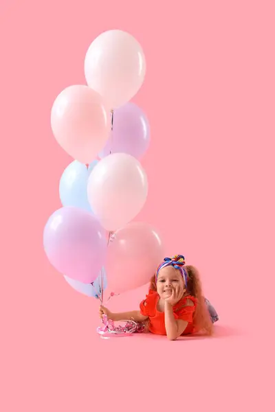 Cute little girl with beautiful balloons lying on pink background