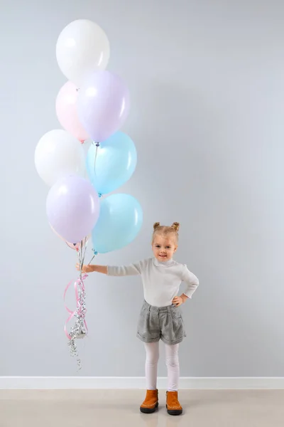 Cute little girl with beautiful balloons near grey wall