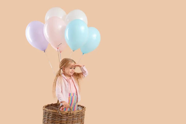 Cute little girl with beautiful balloons and wicker bucket on beige background