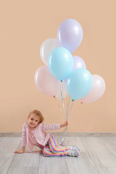 Cute little girl with beautiful balloons sitting near beige wall