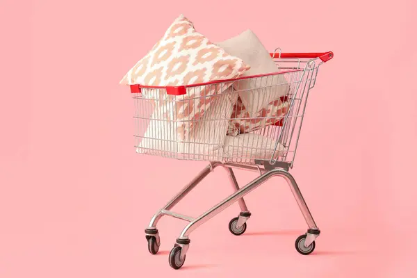 Shopping cart with cushions on pink background