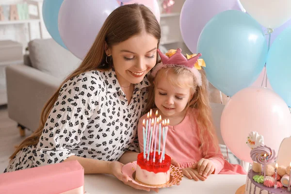 Cute little girl in crown with her mother and cake celebrating Birthday at home