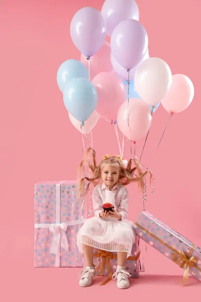 Cute little girl with Birthday muffin, balloons and gifts on pink background