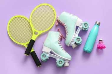 Tenis raketleri, patenler, mekik horozu ve renkli arka planda bir şişe su.