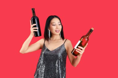 Kırmızı arka planda şarap şişeleri olan güzel Asyalı kadın.