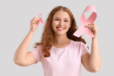 Açık arkaplanda pembe kurdeleli genç bir kızıl kadın. Göğüs kanseri farkındalığı konsepti