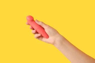 Sarı arka planda vibratörü olan kadın el, yakın plan.