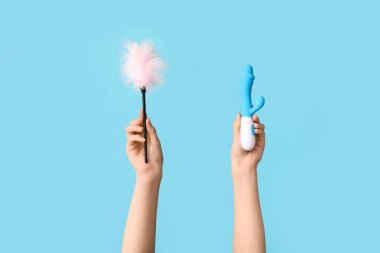 Vibratörlü kadın elleri ve arka planda seks dükkanından tüy çubuğu.