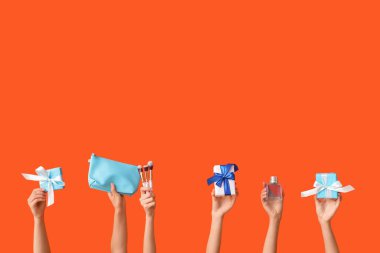 Farklı kozmetik ürünlere sahip kadın elleri ve turuncu arka planda hediyeler