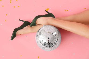 Disko topu ve pembe arka planda konfeti olan şık topuklu kadın bacakları.
