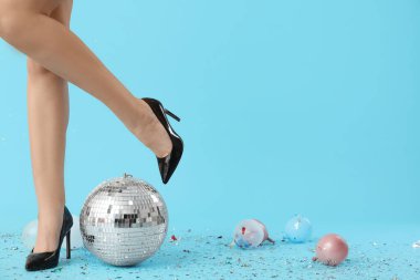 Şık topuklu kadın bacakları, disko topu ve mavi arka planda konfeti.