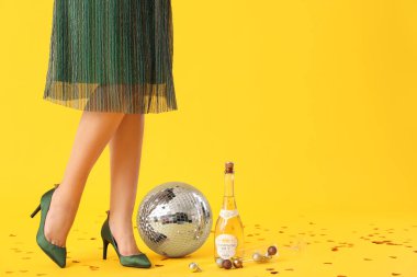Disko topu ve sarı arka planda bir şişe şampanyası olan güzel genç bir kadın.
