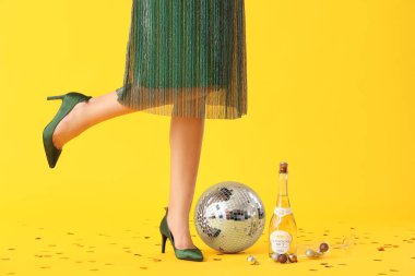 Disko topu ve sarı arka planda bir şişe şampanyası olan güzel genç bir kadın.