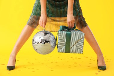 Disko topu ve sarı arka planda hediyeleri olan güzel genç bir kadın.