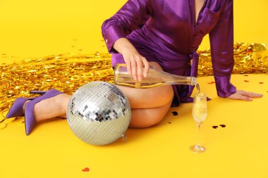 Disko topu ve sarı arka planda bir şişe şampanyası olan güzel genç bir kadın.