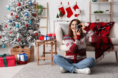 Noel için dekore edilmiş odada fotoğraf çeken güzel, genç ve mutlu bir kadın.