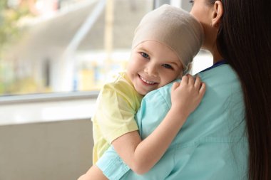 Kemoterapiden sonra küçük kız klinikte sarılan hemşire, yakın plan.