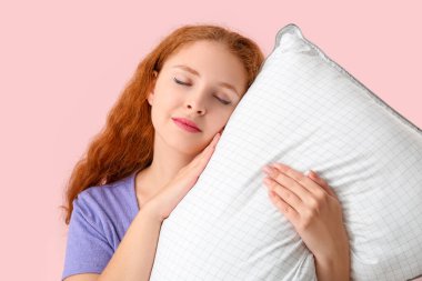 Pembe arka planda beyaz yumuşak yastıklı güzel bir kadın.