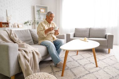 Evdeki kanepede oturan çaylı yaşlı kadın.