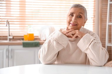 Mutfakta masada oturan kıdemli kadın.