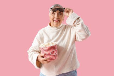 Pembe arka planda 3 boyutlu gözlüklü ve patlamış mısırlı yaşlı kadın.