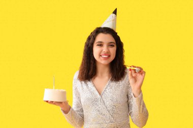 Parti düdüğü ve tatlı pastasıyla güzel genç bir kadın sarı arka planda doğum gününü kutluyor.