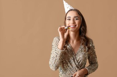 Kahverengi arka planda parti düdüğü çalan güzel genç bir kadın doğum gününü kutluyor.