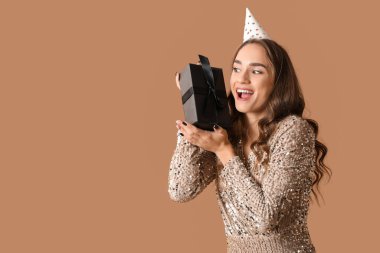 Parti şapkalı güzel bir kadın kahverengi arka planda doğum gününü kutluyor.