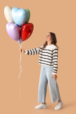 Kahverengi arka planda kalp şeklinde balonları olan güzel genç bir kadın.