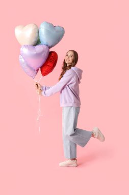 Pembe arka planda kalp şeklinde balonları olan güzel genç bir kadın.