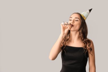 Gri arka planda parti düdüğüyle doğum gününü kutlayan güzel genç bir kadın.